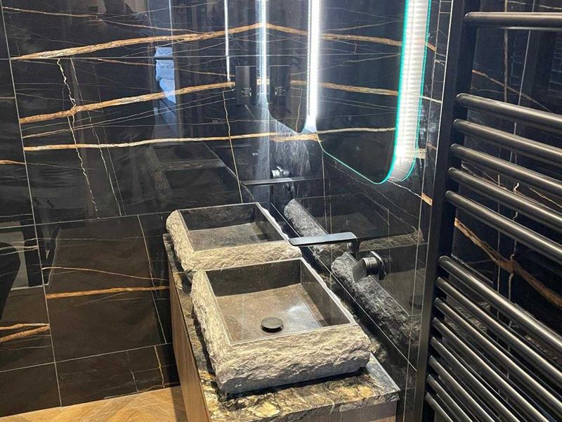 Dark marble bathroom with backlit detailing and a stone basin on a timber vanity