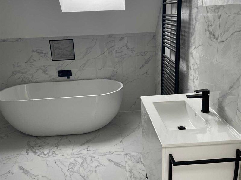 Marble tiled bathroom with a freestanding bath, basin unit and black heated towel rail