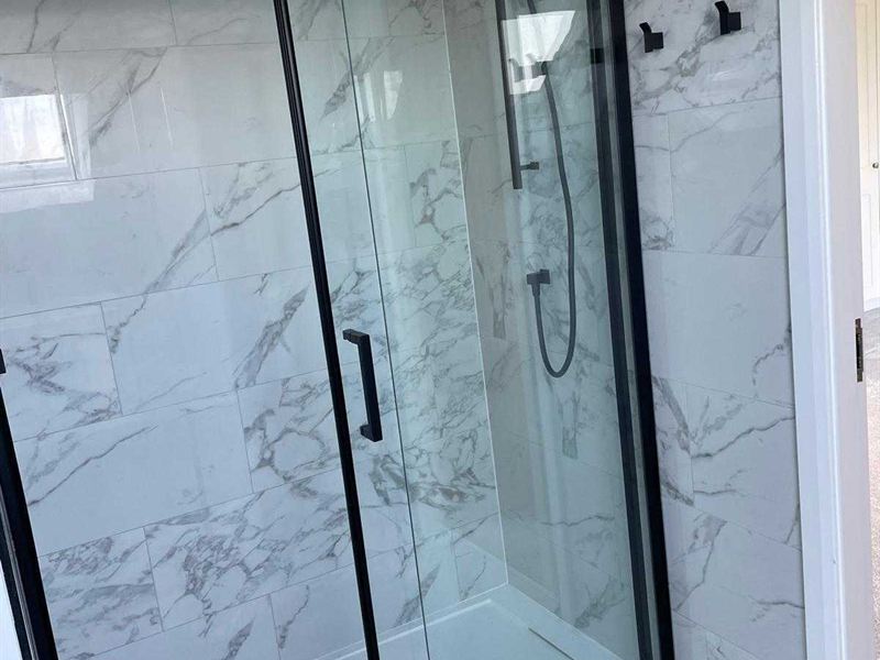 Walk-in shower with black framed sliding glass against marble effect tiling