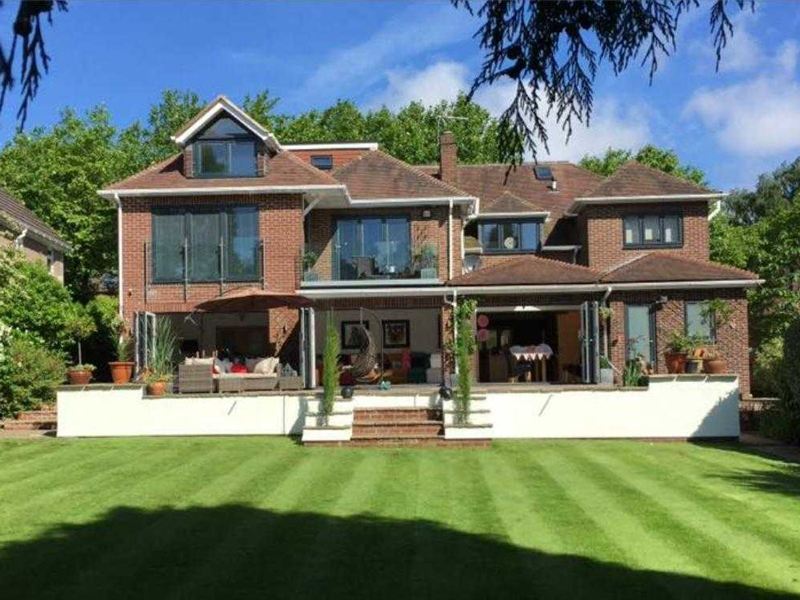 Two storey brick rear extension with bi-fold doors and a balcony, opening onto a striped lawn