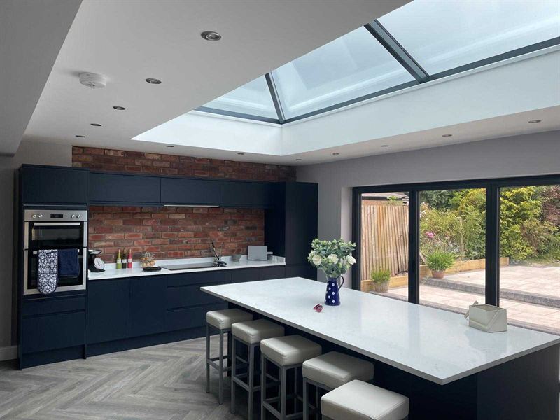 Navy kitchen in a rear extension, lit by a roof lantern, with an exposed brick feature wall