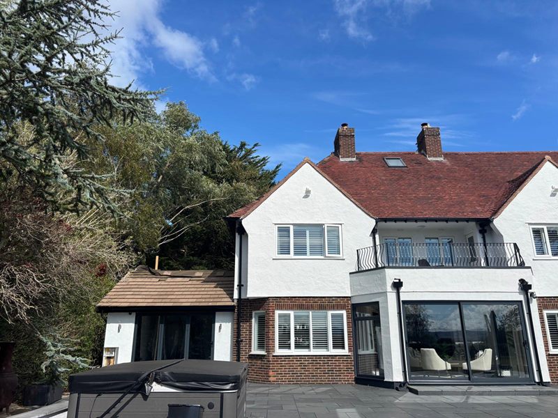 Rear of a large rendered house with a first floor balcony, full height glazing and a new single storey extension