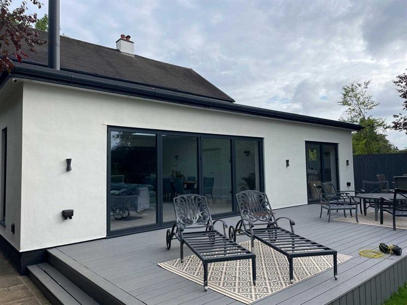 White rendered single storey rear extension with grey composite decking and garden furniture