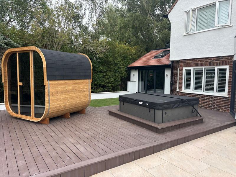 Composite decking laid around a barrel sauna and a sunken hot tub, alongside a porcelain patio