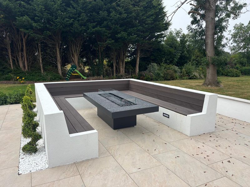 Sunken seating area with rendered walls, composite timber benches and a gas firepit table on porcelain paving