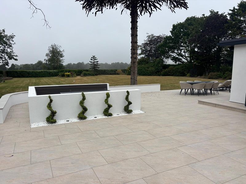 Rendered garden wall planted with spiral topiary in white gravel, beside a curved bench and a paved terrace