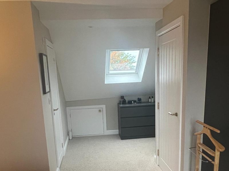 Loft room finished in soft neutrals with a roof window, a fitted eaves storage hatch and a chest of drawers