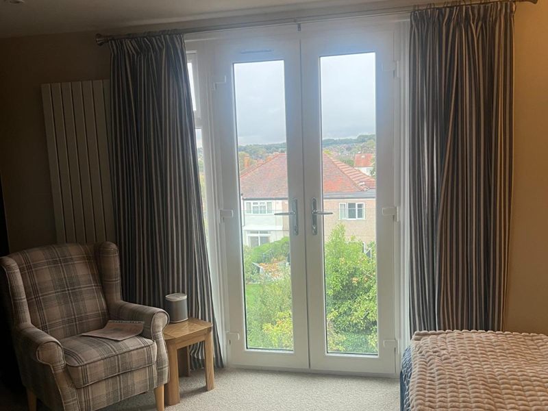 Loft bedroom with full height French doors onto a Juliet balcony, an armchair and views over neighbouring rooftops