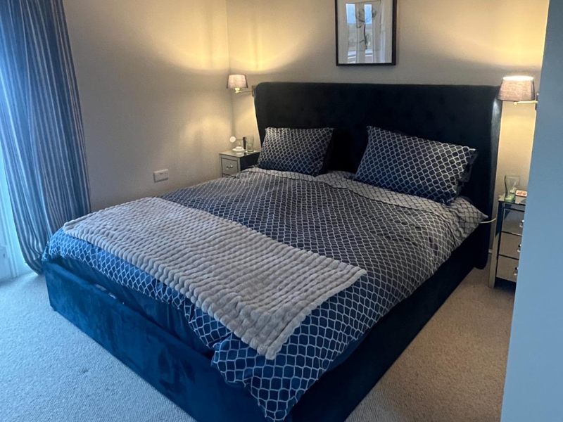 Completed loft bedroom with a king size bed, navy velvet headboard and brass wall lights either side