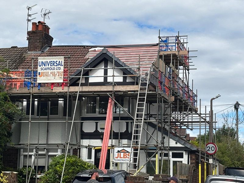 Scaffolded front elevation of a Heswall semi with the roof stripped back and a JLBS Construction site board
