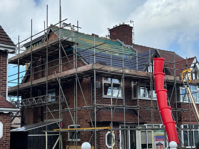 Roof part way through being re-covered on a loft conversion, with a red rubbish chute and scaffolding