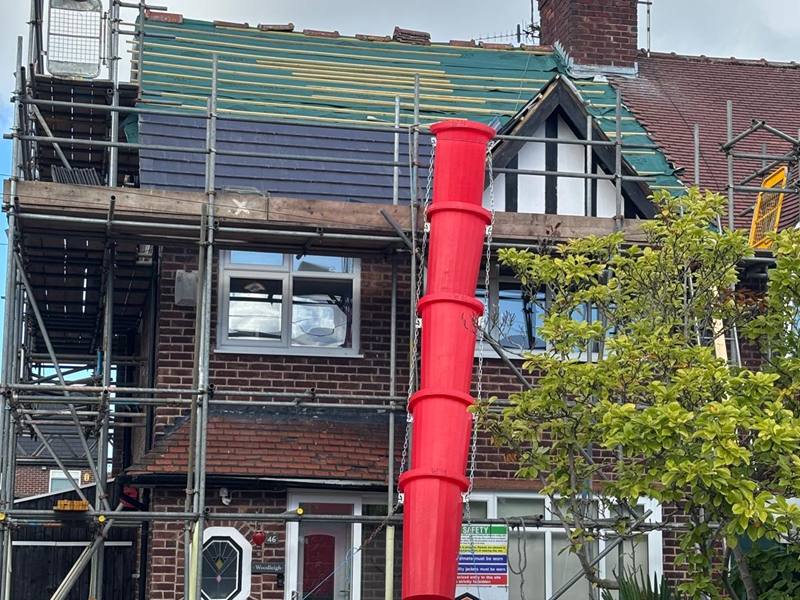 Roof stripped back to the battens and membrane on a loft conversion, with a red rubbish chute down to a skip