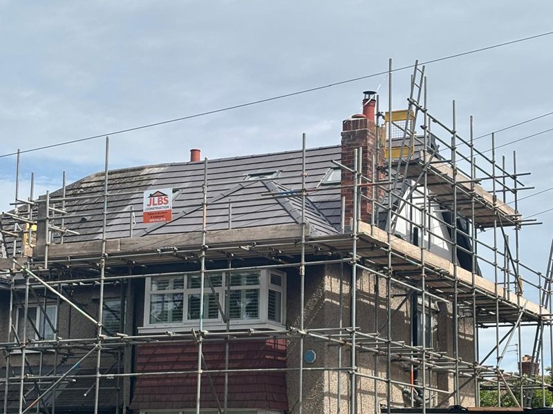Loft conversion under way behind scaffolding, with a new tiled roof and a JLBS Construction site board