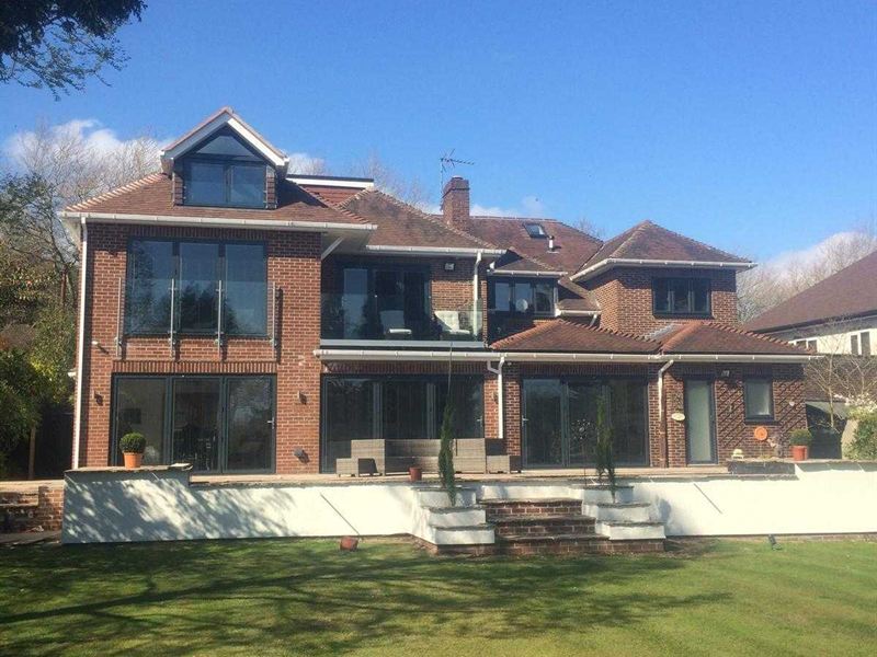 Modern brick new build with glass balconies overlooking a lawned garden