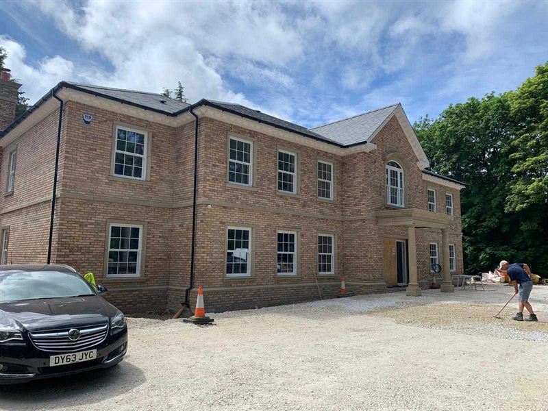 Large detached new build house in buff brick with sash windows and a stone portico, nearing completion
