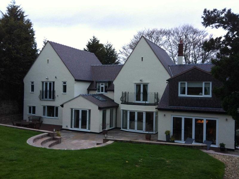 Large white rendered new build house with multiple gables and a paved terrace to the rear