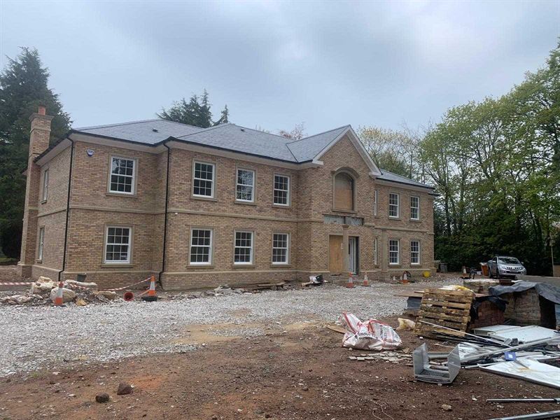 New build house part way through construction, with brickwork and slate roof complete ahead of landscaping