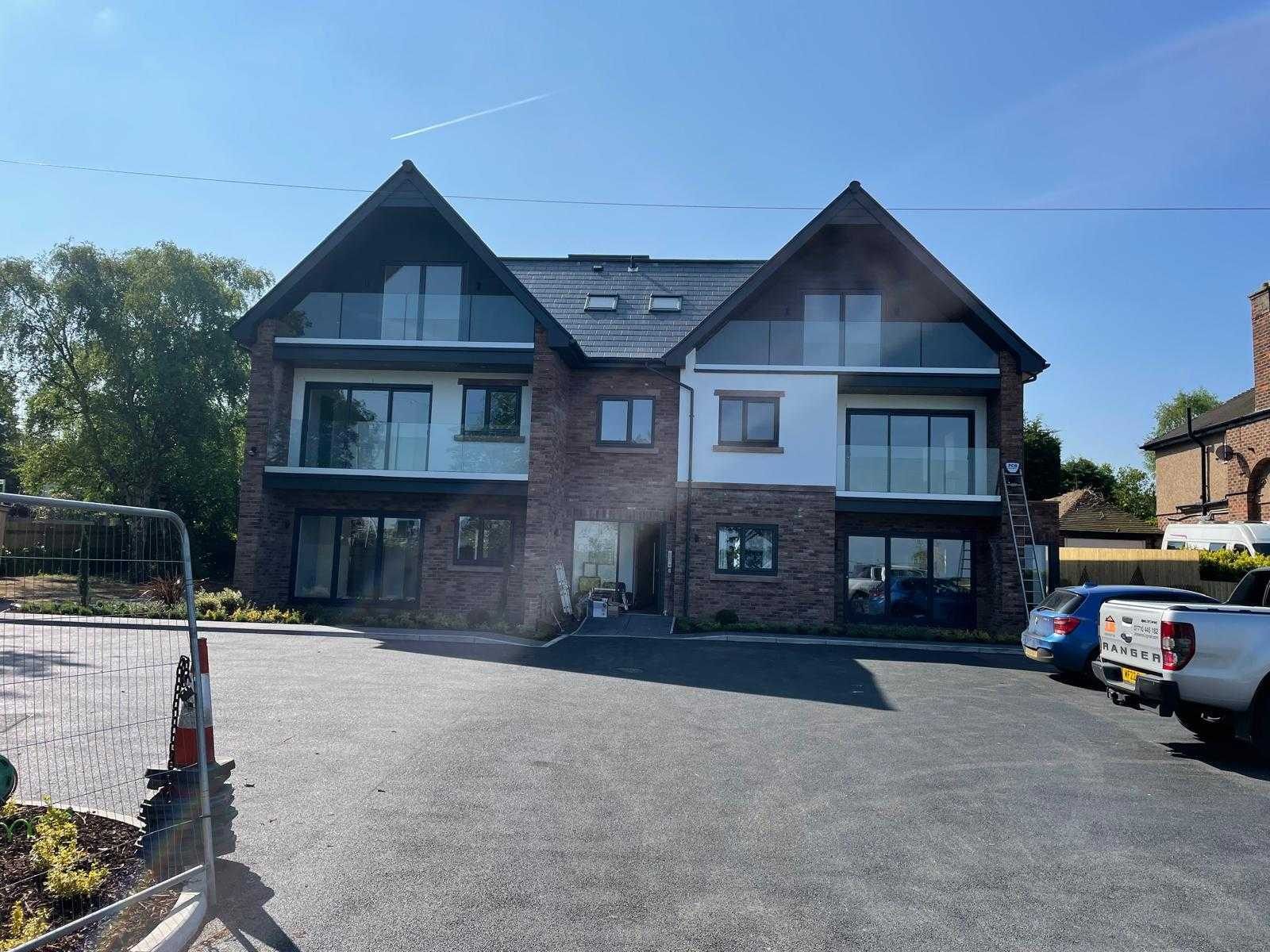 The completed replacement building: two modern homes in brick and render with glass balconies and a new tarmac driveway